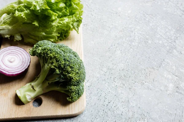 Vegetais verdes frescos maduros na tábua de corte na superfície de concreto cinza — Fotografia de Stock