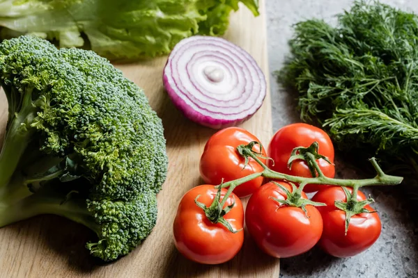 Verduras frescas maduras en la tabla de cortar en la superficie de hormigón gris - foto de stock