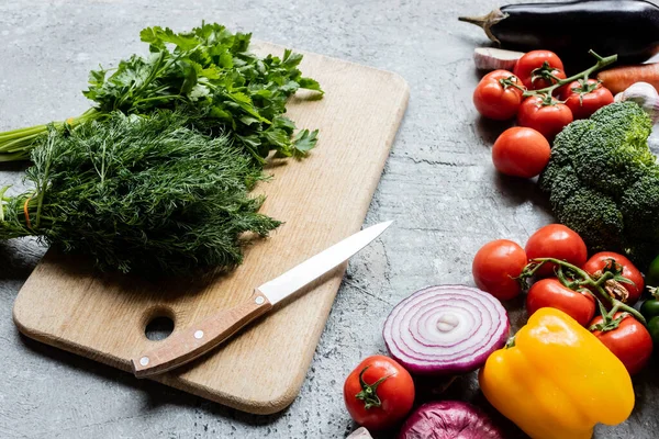 Buntes frisches reifes Gemüse am Schneidebrett mit Messer auf grauer Betonoberfläche — Stockfoto