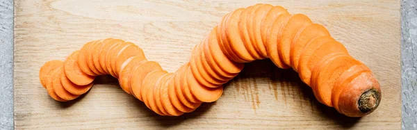 Vue de dessus des tranches fraîches de carotte mûre sur la planche à découper en bois sur la surface du béton, culture panoramique — Photo de stock