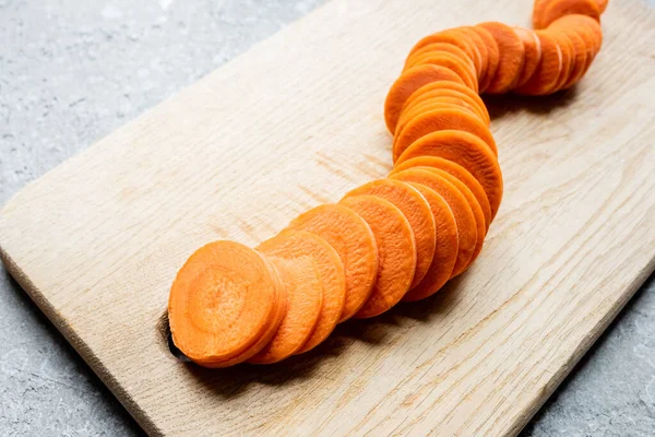 Fresh ripe carrot slices on wooden cutting board on concrete surface — Stock Photo