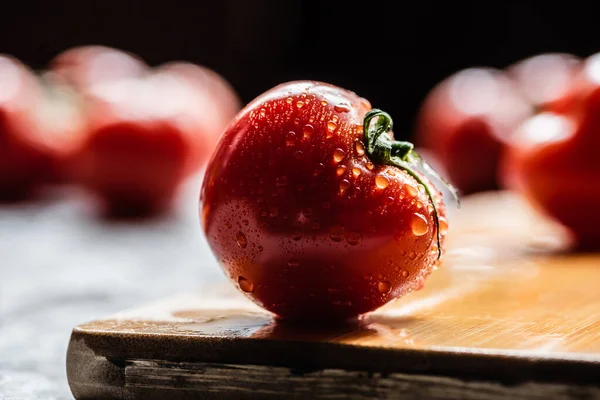 Foco seletivo de tomate vermelho maduro fresco com gotas de água em tábua de madeira isolada em preto — Fotografia de Stock