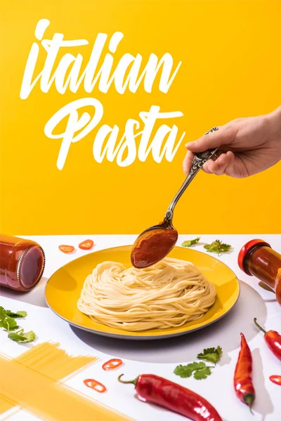 Обрезанный вид женщины, добавляющей кетчуп к спагетти на белой поверхности, изолированный на желтой, итальянской макаронной иллюстрации — стоковое фото