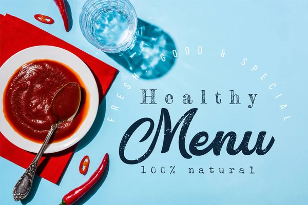 Delicious chili sauce in pate on red napkin beside glass of water and chili peppers on blue surface, healthy menu illustration — Stock Photo