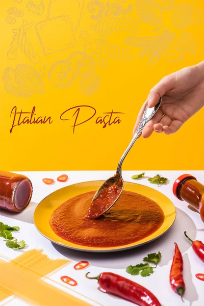 Cropped view of woman holding spoon with ketchup with spaghetti and chili peppers on white surface isolated on yellow, Italian pasta illustration — Stock Photo
