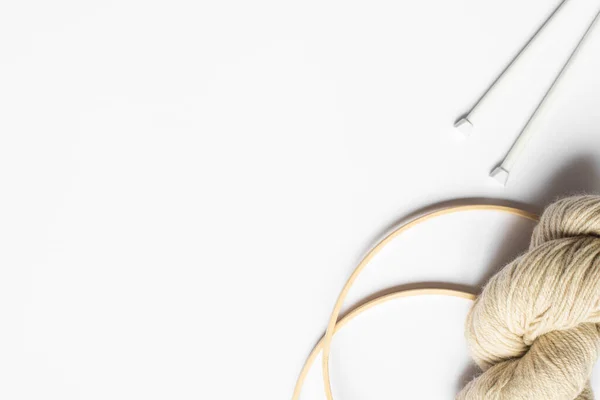 Top view of beige yarn and knitting needles and looms on white background with copy space — Stock Photo