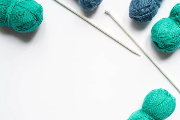 Vue du dessus des fils de laine bleus et verts et des aiguilles à tricoter sur fond blanc — Photo de stock