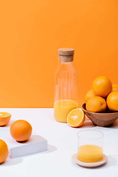 Fresh orange juice in glass and bottle near oranges in bowl on white surface isolated on orange — Stock Photo