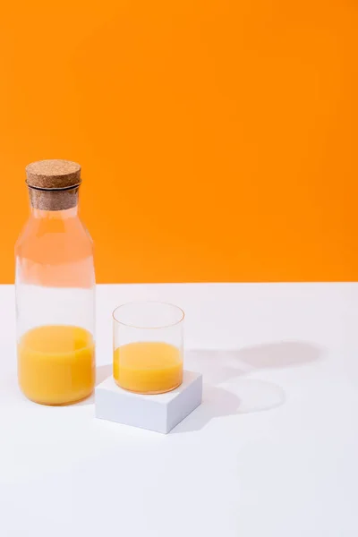 Jus d'orange frais en verre et bouteille sur surface blanche isolé sur orange — Photo de stock