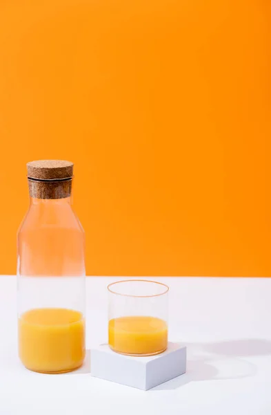 Suco de laranja fresco em vidro e garrafa na superfície branca isolada em laranja — Fotografia de Stock