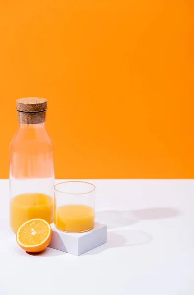 Jus d'orange frais en verre et bouteille près de fruits coupés sur surface blanche isolé sur orange — Photo de stock