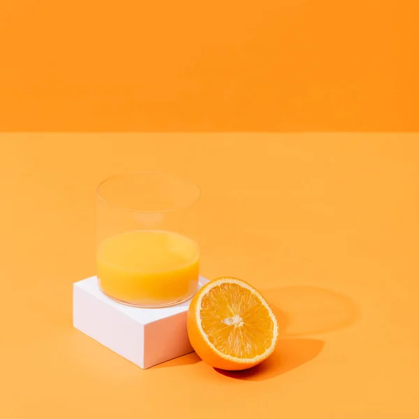 Свежий апельсиновый сок в стакане около половины апельсина и белого куба изолированы на оранжевый — стоковое фото