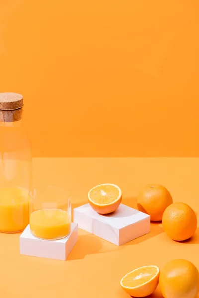 Fresh orange juice in glass and bottle near ripe oranges and white cubes isolated on orange — Stock Photo