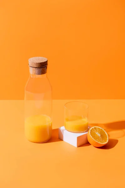 Zumo de naranja fresco en vidrio y botella cerca de la mitad del cubo de naranja y blanco aislado en naranja - foto de stock