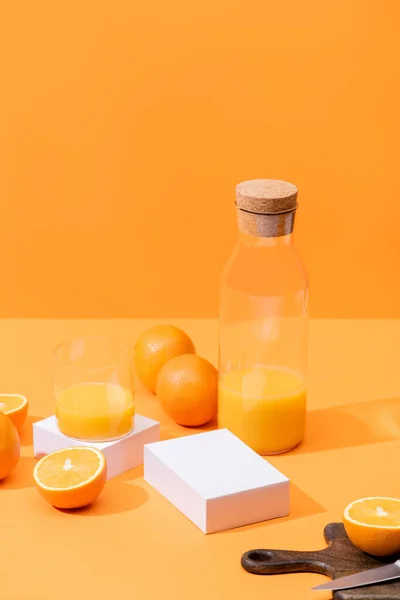 Fresh orange juice in glass and bottle near ripe oranges, wooden cutting board with knife isolated on orange — Stock Photo