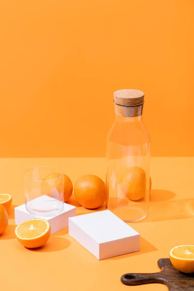 Jus d'orange frais en verre et bouteille près d'oranges mûres, planche à découper en bois isolée sur orange — Photo de stock