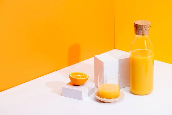 Fresh orange juice in glass and bottle near ripe orange on white surface on orange background — Stock Photo