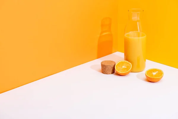 Frischer Orangensaft in Glasflasche in der Nähe reifer Orangen und Korken auf weißer Oberfläche auf orangefarbenem Hintergrund — Stockfoto