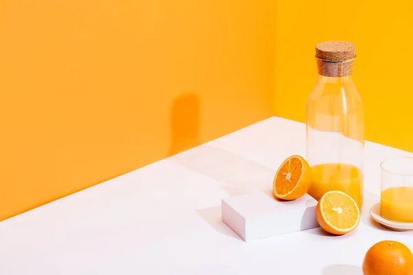 Frischer Orangensaft in Glas und Flasche nahe reifer Orangen auf weißer Oberfläche auf orangefarbenem Hintergrund — Stockfoto