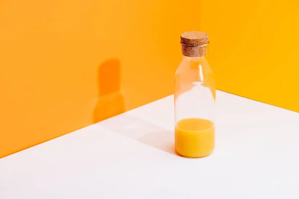 Succo d'arancia fresco in bottiglia di vetro su superficie bianca su sfondo arancione — Foto stock