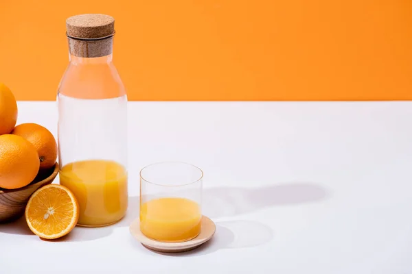 Suco de laranja fresco em vidro e garrafa perto de laranjas em tigela de madeira na superfície branca isolada em laranja — Fotografia de Stock