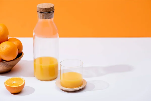 Fresh orange juice in glass and bottle near oranges in wooden bowl on white surface isolated on orange — Stock Photo