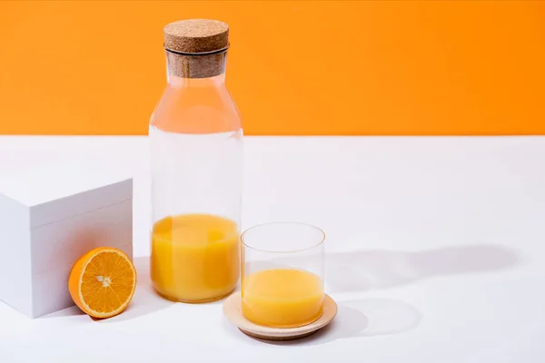 Zumo de naranja fresco en vidrio y botella cerca de la mitad de naranja madura en la superficie blanca aislada en naranja - foto de stock