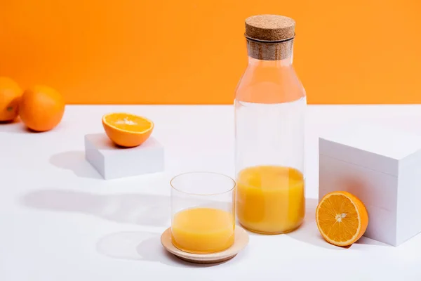 Zumo de naranja fresco en vidrio y botella cerca de naranjas maduras en superficie blanca aislada en naranja - foto de stock