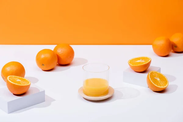 Jus d'orange frais en verre près d'oranges mûres sur surface blanche isolé sur orange — Photo de stock