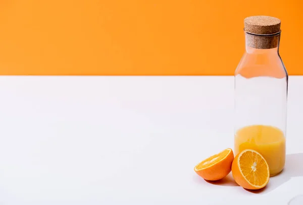 Jus d'orange frais en bouteille près des moitiés orange mûre sur surface blanche isolée sur orange — Photo de stock