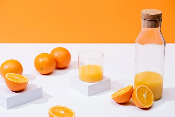 Jus d'orange frais en verre et bouteille près d'oranges mûres sur surface blanche isolée sur orange — Photo de stock