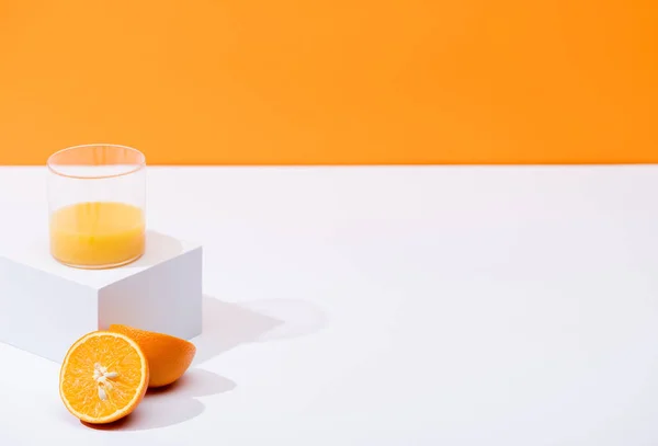 Zumo de naranja fresco en vaso cerca de naranjas maduras en superficie blanca aislada en naranja - foto de stock