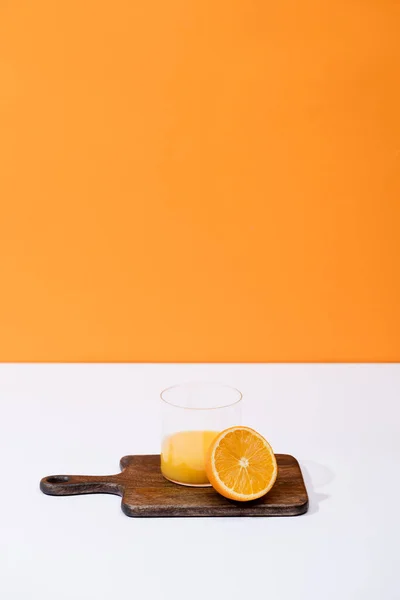Fresh orange juice in glass near cut fruit on wooden cutting board on white surface isolated on orange — Stock Photo