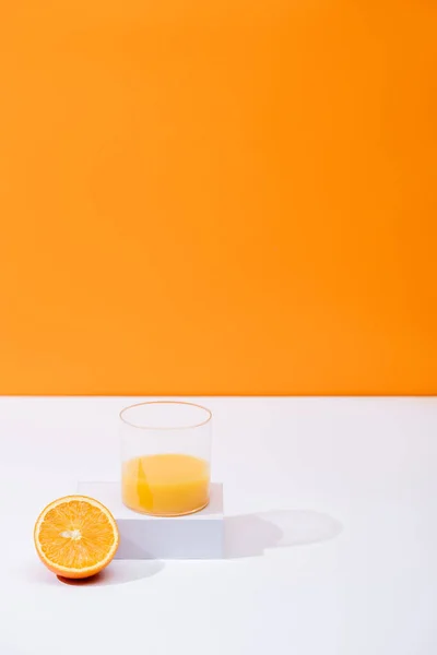 Jus d'orange frais en verre près de fruits coupés sur surface blanche isolé sur orange — Photo de stock