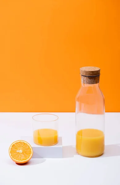 Suco de laranja fresco em vidro e garrafa com cortiça perto de frutas cortadas na superfície branca isolada em laranja — Fotografia de Stock