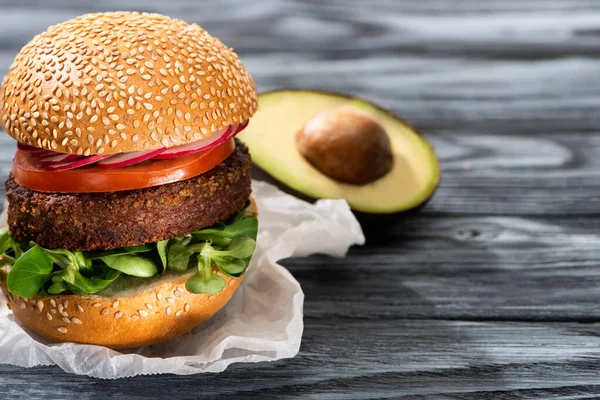 Enfoque selectivo de sabrosa hamburguesa vegana con rábano servido en la mesa de madera con aguacate mitad - foto de stock