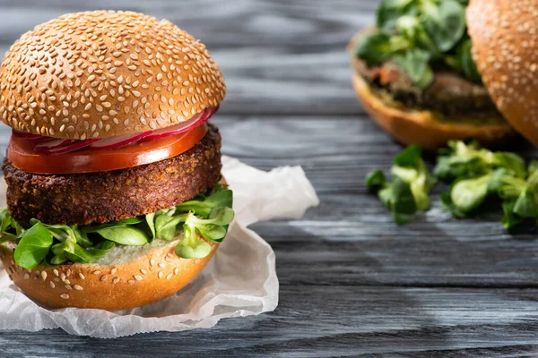 Enfoque selectivo de sabrosas hamburguesas veganas con microgreens y verduras servidas en mesa de madera - foto de stock