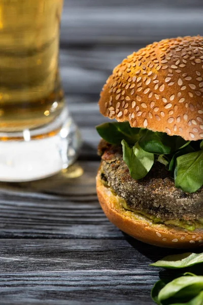 Foco seletivo de hambúrguer vegan saboroso com microgreens servidos em mesa de madeira com copo de cerveja — Fotografia de Stock