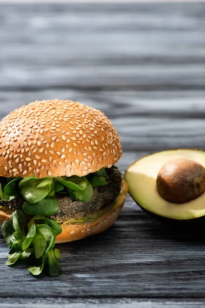 Hambúrguer vegan saboroso com microgreens servido em mesa de madeira com metade de abacate — Fotografia de Stock
