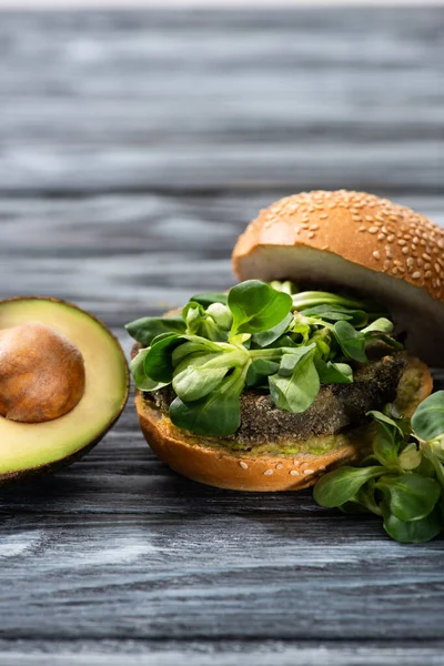 Tasty vegan burger with microgreens served on wooden table with avocado half — Stock Photo