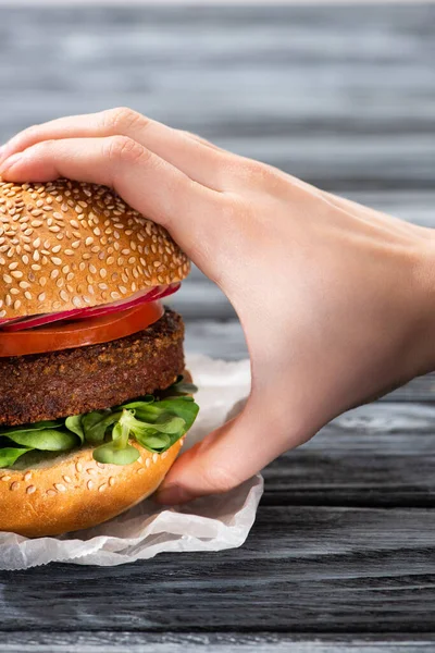 Vue recadrée de la main féminine avec hamburger végétalien savoureux sur table en bois — Photo de stock