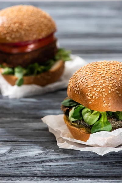 Enfoque selectivo de sabrosas hamburguesas veganas con microgreens servidos en mesa de madera - foto de stock