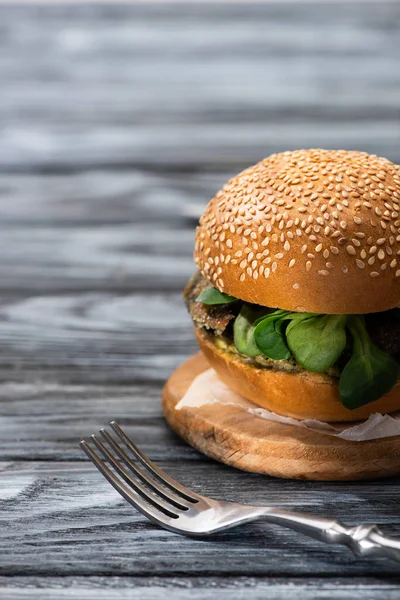 Tasty vegan burger with microgreens served on wooden table with fork — Stock Photo