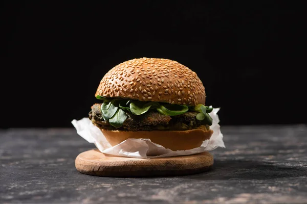 Tasty vegan burger with microgreens served on wooden board isolated on black — Stock Photo