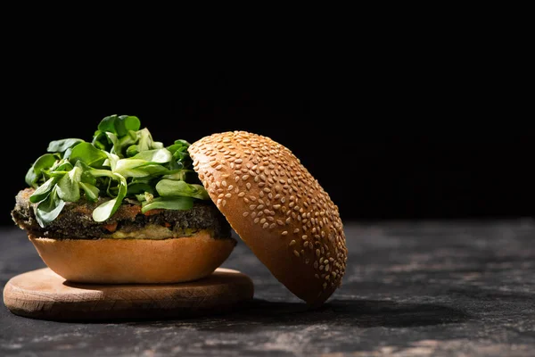 Tasty vegan burger with microgreens served on wooden board isolated on black — Stock Photo