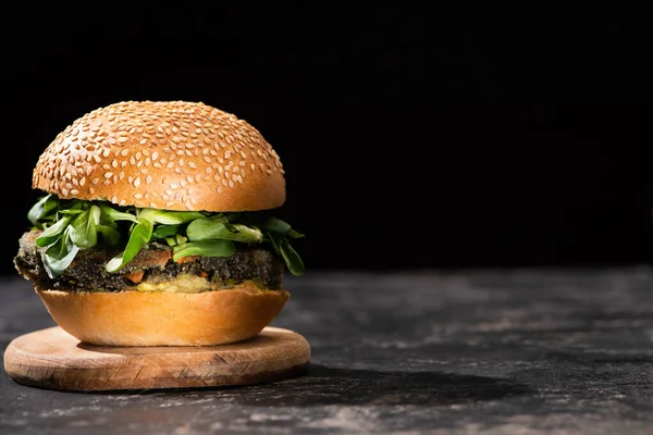 Tasty vegan burger with microgreens served on wooden board isolated on black — Stock Photo