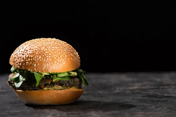 Tasty vegan burger with microgreens served on textured surface isolated on black — Stock Photo
