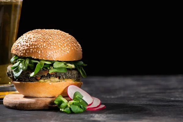 Foyer sélectif de hamburger végétalien savoureux avec microgreens servis avec de la bière et du radis sur surface texturée isolé sur noir — Photo de stock