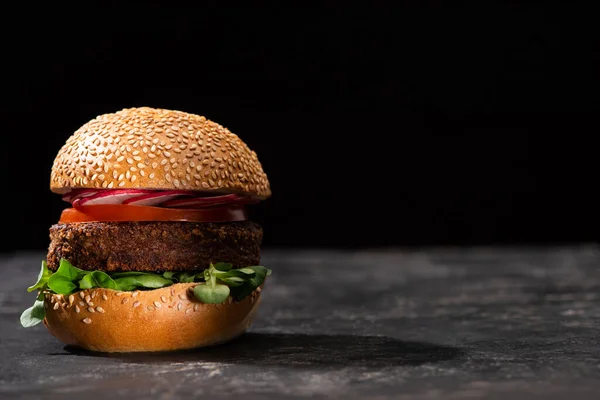 Sabrosa hamburguesa vegana con microgreens, rábano y tomate servido en la superficie texturizada aislado en negro - foto de stock