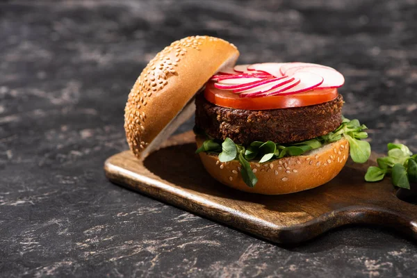 Tasty vegan burger with vegetables served on wooden cutting board on textured surface — Stock Photo